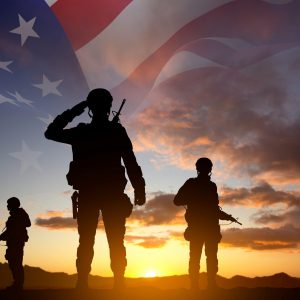 Silhouettes of a soldiers with USA flag against the sunset. Veterans Day. Honoring All Who Served