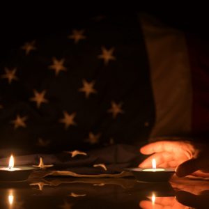 A reflective scene with lit candles and an American flag, symbolizing honor, sacrifice, and remembrance in a solemn tribute.
