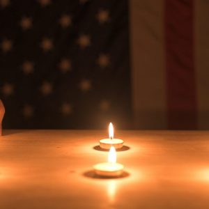 A hand lights a candle on a wooden table, symbolizing remembrance, unity, and patriotism, with an American flag in the background. Concept of remembrance, celebration.